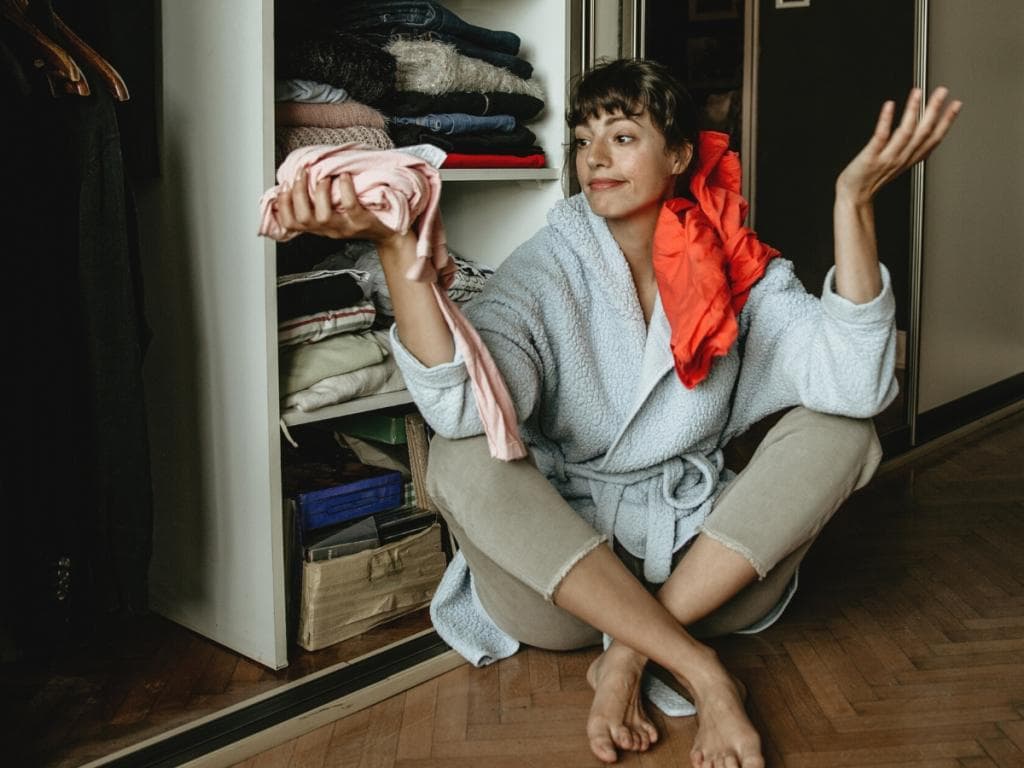 En kvinne som sitter på gulvet, holder et par bukser i hendene og ser tankefull ut