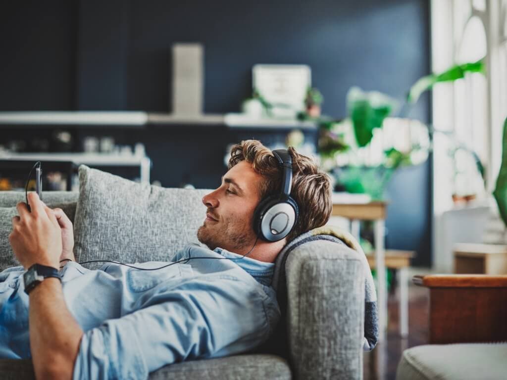 En mann slapper av på en sofa, lytter til musikk gjennom hodetelefoner, med et fredfullt uttrykk i ansiktet